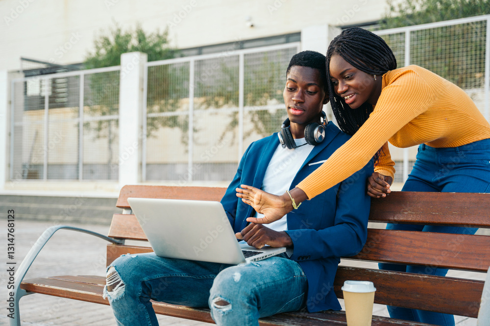 Young black colleagues working on laptop outdoors