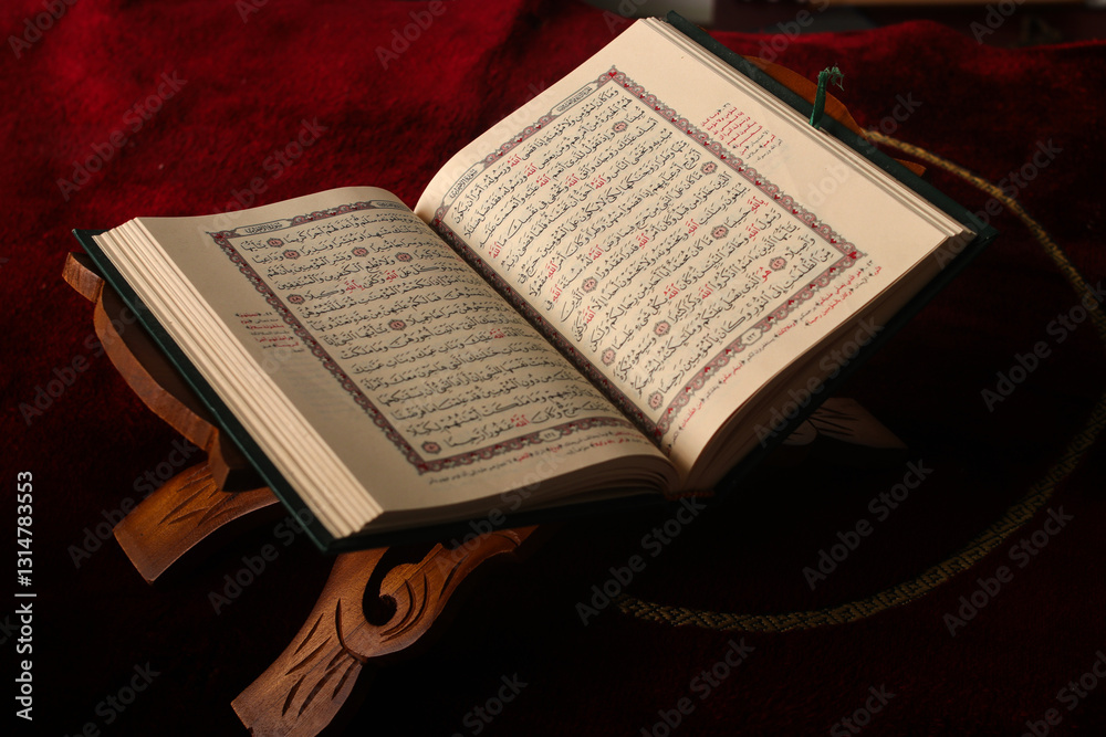 Fototapeta premium An open Quran on a wooden stand against a rich red prayer mat background. The pages display intricate Arabic calligraphy, suitable for themes of spirituality and Islamic culture