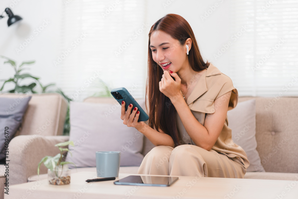 Asian Businesswoman Sitting on Sofa, Smiling While Using Smartphone With Earbuds, Surrounded by Cozy Living Room. Asian Businesswoman Sitting on Sofa, Smiling While Using Smartphone With Earbuds, Surrounded by Cozy Living Room.