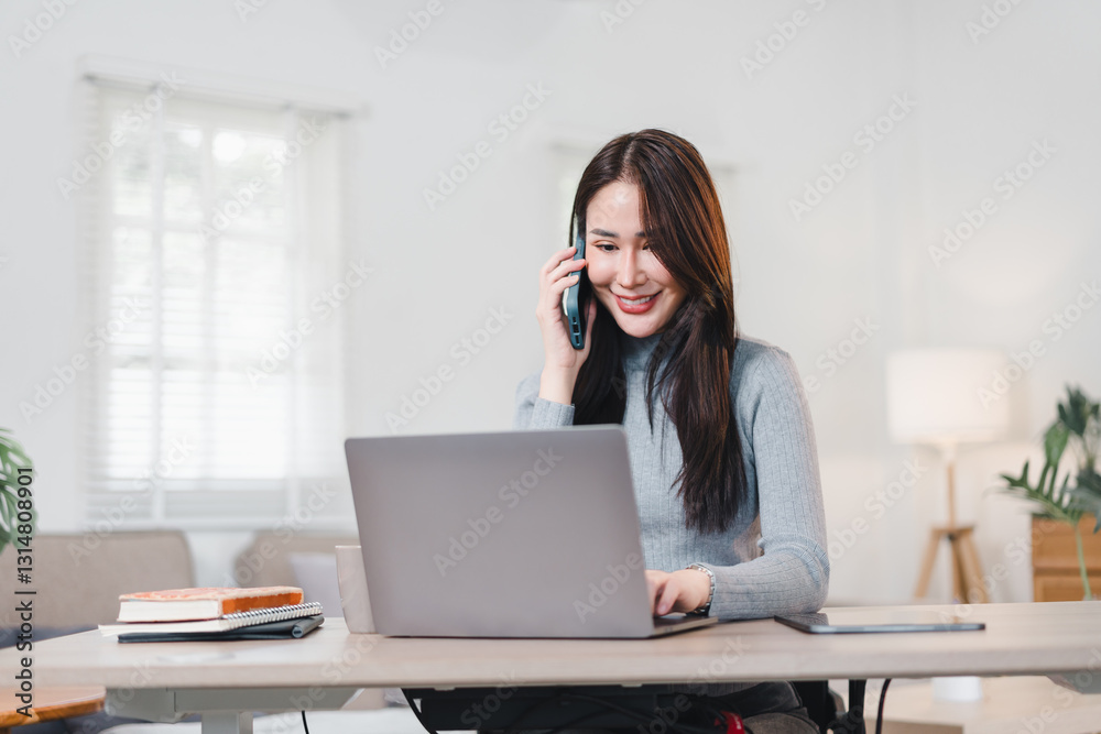 Asian Businesswoman Working From Home, Smiling While Talking on Phone and Using Laptop in Bright, Modern Living Room. Asian Businesswoman Working From Home, Smiling While Talking on Phone and Using Laptop in Bright, Modern Living Room.