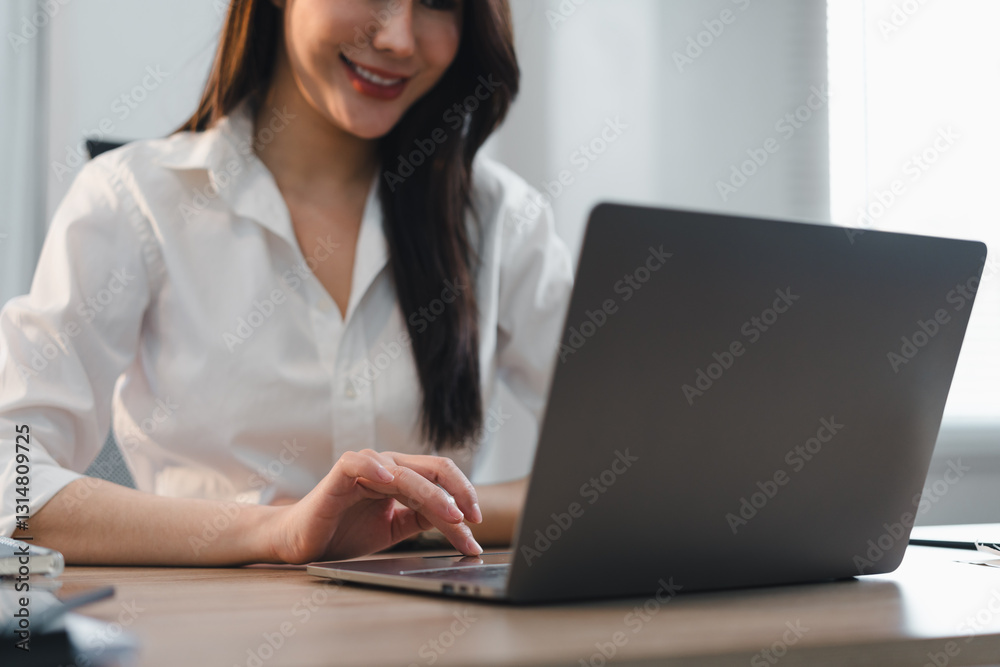 Asian Businesswoman in White Shirt Working on Laptop at Wooden Desk, Smiling and Focused. Asian Businesswoman in White Shirt Working on Laptop at Wooden Desk, Smiling and Focused.