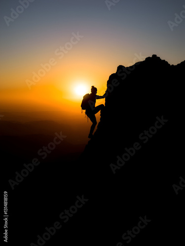Silhouette of climber ascending rocky hill at sunset, evoking adventure and determination