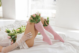 Elegant woman in lingerie lying on a bed with fresh tulips, wearing sheer gloves and pink socks, in a bright, minimalistic interior