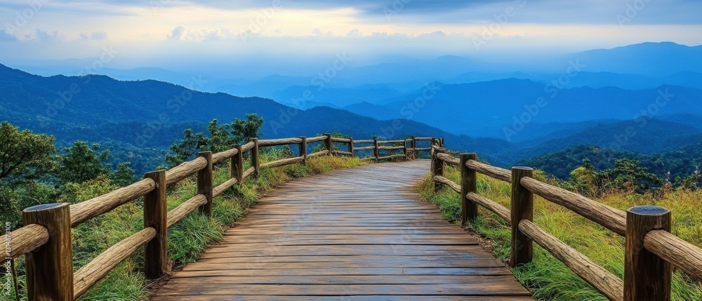 Obraz premium Serene vista from wooden path overlooking misty blue mountain range under cloudy sky in summer