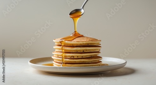 Delicious pancakes with honey dripping from a spoon on a plate.