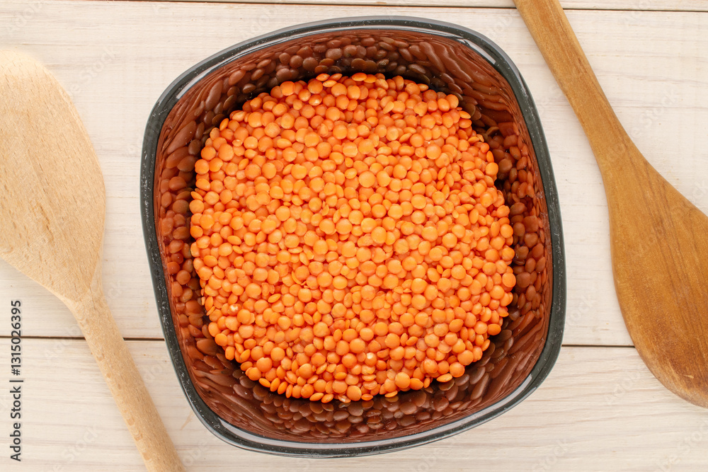 Red lentils in a ceramic plate with a wooden spoon on a wooden table, close-up, top view. Red lentils in a ceramic plate with a wooden spoon on a wooden table, close-up, top view.
