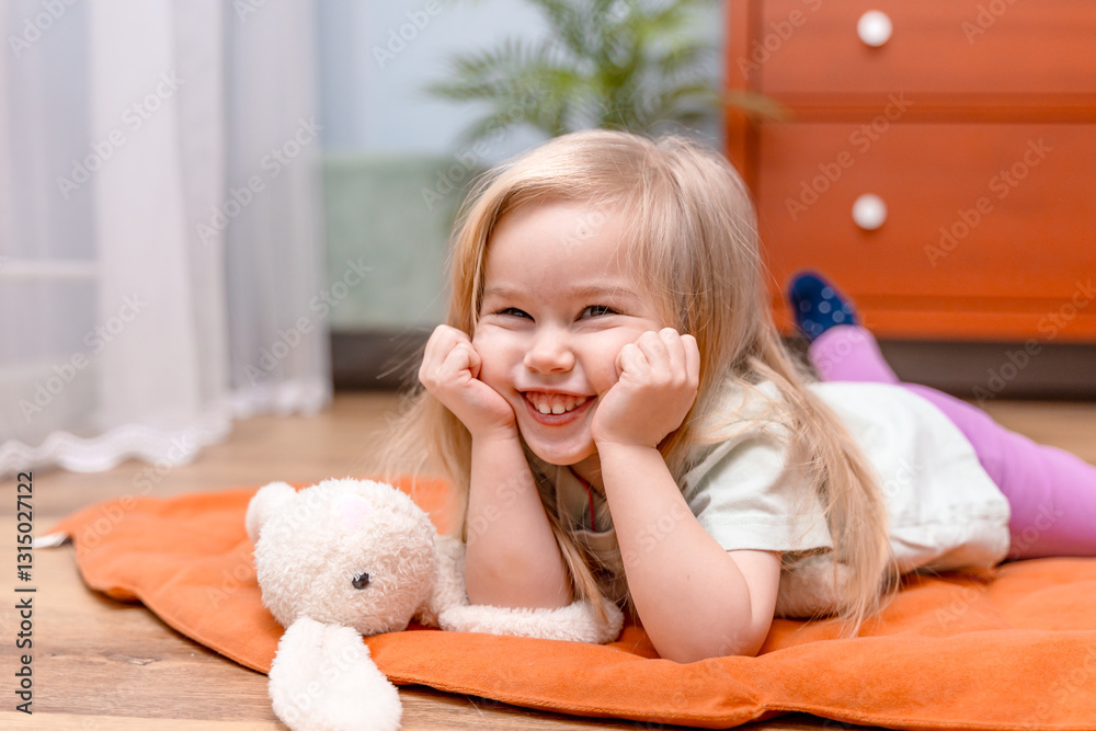 A blonde-haired child, a three-year-old girl, is lying on the floor with a bunny toy in the room A blonde-haired child, a three-year-old girl, is lying on the floor with a bunny toy in the room