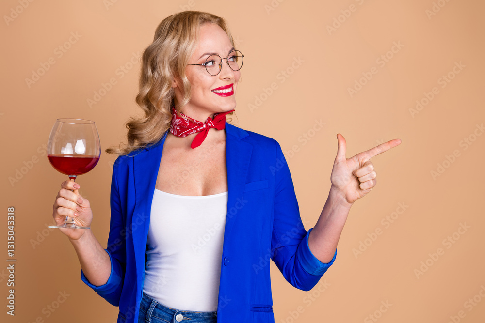 Elegant Woman Wearing Blue Jacket Holding Wine Glass and Pointing with Her Finger Against Beige Background Elegant Woman Wearing Blue Jacket Holding Wine Glass and Pointing with Her Finger Against Beige Background