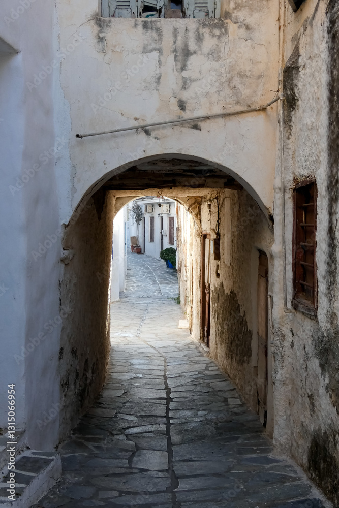 Narrow alley with tunnel and with whitewashed walls and stone pavement leading to a courtyard in the Greek Islands, Greece Narrow alley with tunnel and with whitewashed walls and stone pavement leading to a courtyard in the Greek Islands, Greece