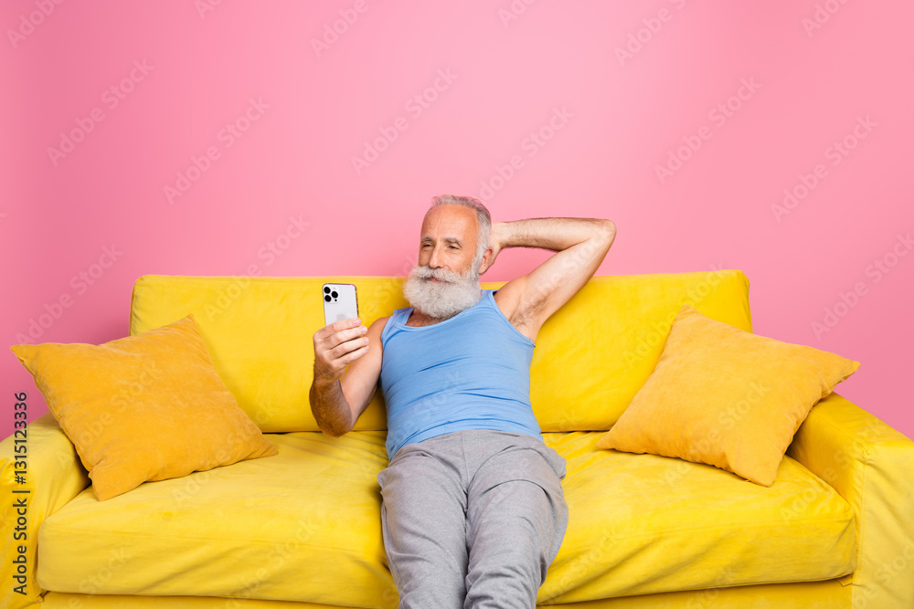 Stylish senior man relaxing on a vibrant yellow sofa in front of a lively pink backdrop Stylish senior man relaxing on a vibrant yellow sofa in front of a lively pink backdrop