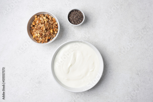 Bowl of greek yogurt, granola and chia seeds on a grey background. Top view with copy space for design elements or text. Plain white yogurt in bowl