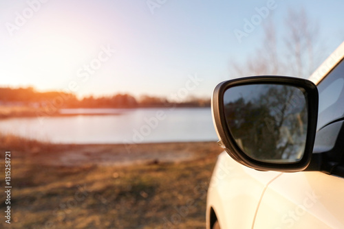 Car side mirror of white car parked aby the lake with clear sky and warm sunlight background.