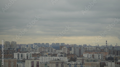 Overcast cityscape with residential buildings and industrial chimneys under a cloudy grey sky
