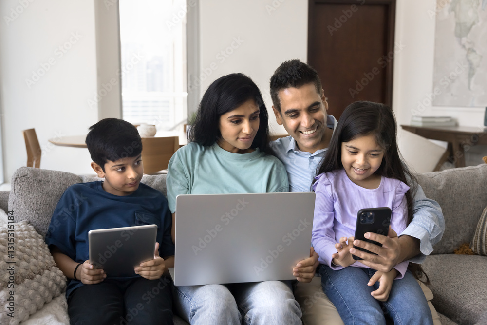 Indian couple and their little son and daughter using diverse modern wireless gadgets seated on couch. Man holds smartphone enjoy new mobile application or game with family, spend leisure on internet Indian couple and their little son and daughter using diverse modern wireless gadgets seated on couch. Man holds smartphone enjoy new mobile application or game with family, spend leisure on internet