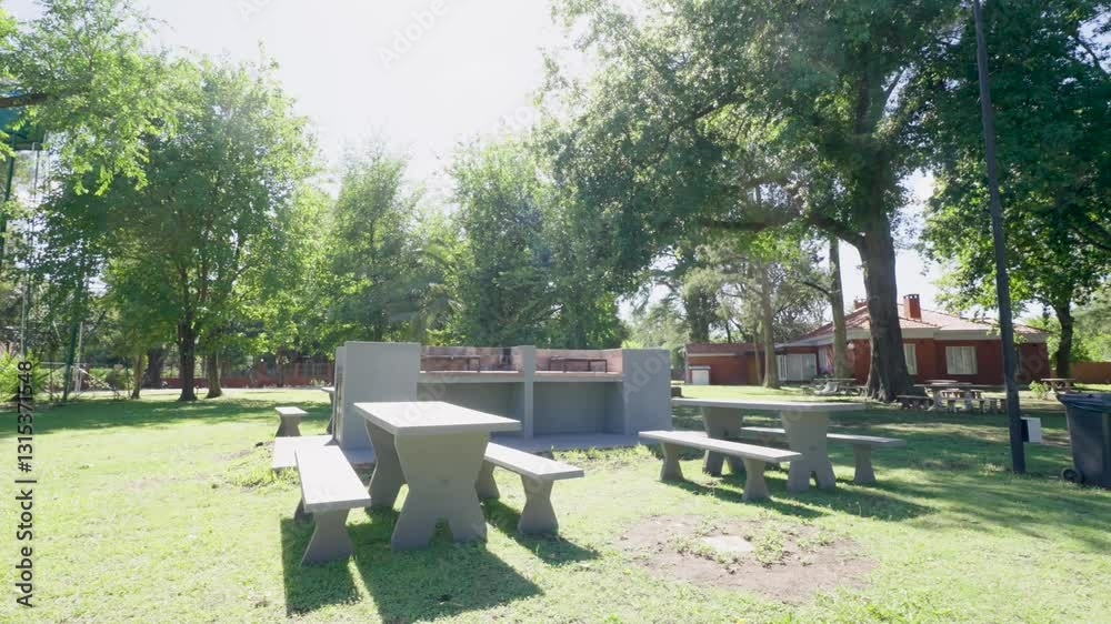 Área de asado y camping en día soleado: parrilla, fuego, mesas de picnic, entorno natural, ambiente relajado y soleado