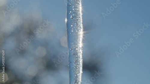 Close-up of a transparent icicle with trapped air bubbles and sunlight reflections against a clear blue sky. Macro shot of frozen water. Winter nature background with copy space for design and print.