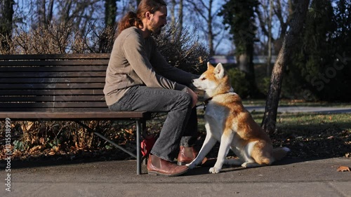 young man petting akita inu dog from the bench in park in autumn