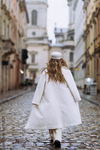 Fototapeta Naklejka Na Ścianę i Meble -  Elegant Woman in a White Coat Walking Through a Historic European Street