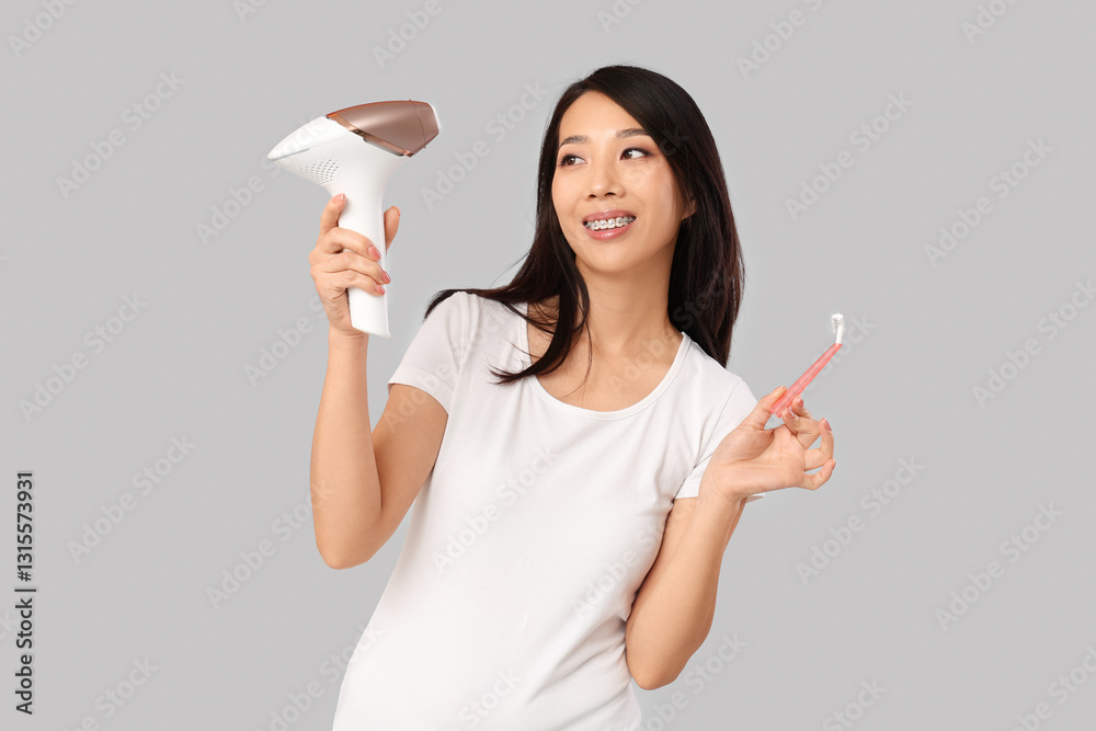 Young Asian woman with photoepilator and razor on grey background Young Asian woman with photoepilator and razor on grey background