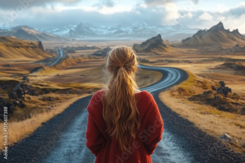 Young woman standing on a winding road overlooking mountains in Iceland during sunset