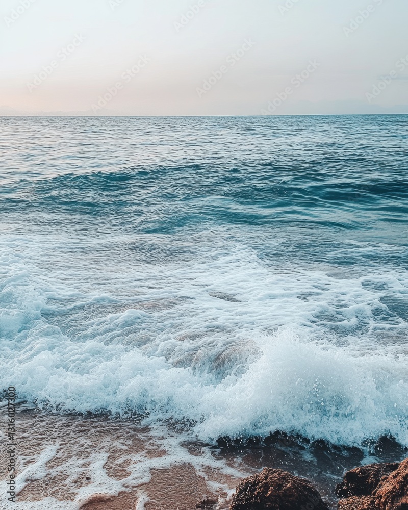 Fototapeta premium Serene ocean vista with gentle waves lapping on sandy beach rocks under a soft pastel sky horizon