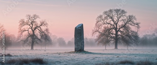 Ancient stone monolith in frosty field at sunrise with trees.
