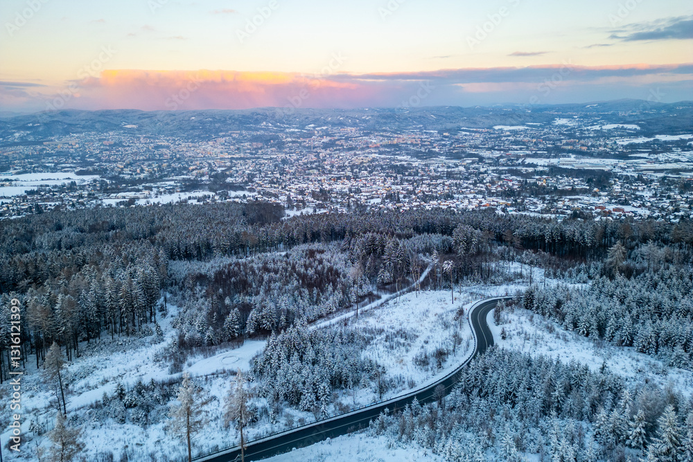 Φωτογραφία A serene winter evening unfolds above Liberec City, showcasing the enchanting snow-covered landscape with winding roads and vibrant pink hues in the sky