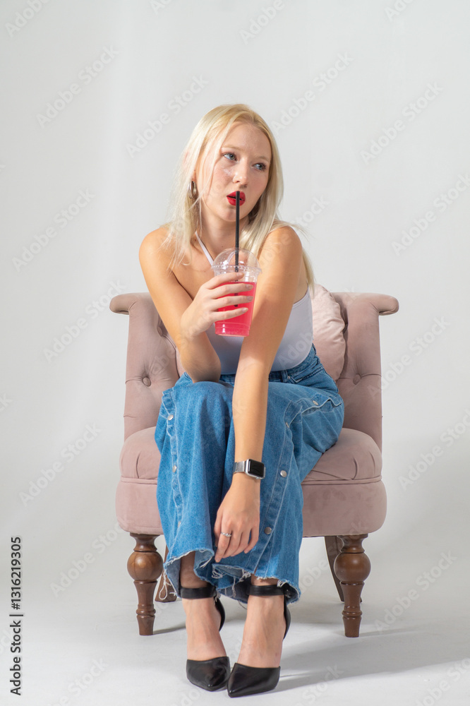 Obraz premium Attractive young blonde holding a pink cocktail. She is wearing a white top and blue jeans on a white background. Copy space