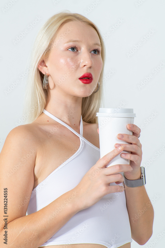 Attractive young blonde holding a papercup with coffee. She is wearing a white top and blue jeans on a white background. Copy space Attractive young blonde holding a papercup with coffee. She is wearing a white top and blue jeans on a white background. Copy space