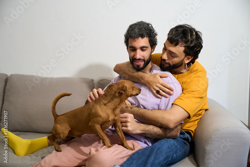 Gay couple embracing on sofa with their dog, sharing a tender moment at home