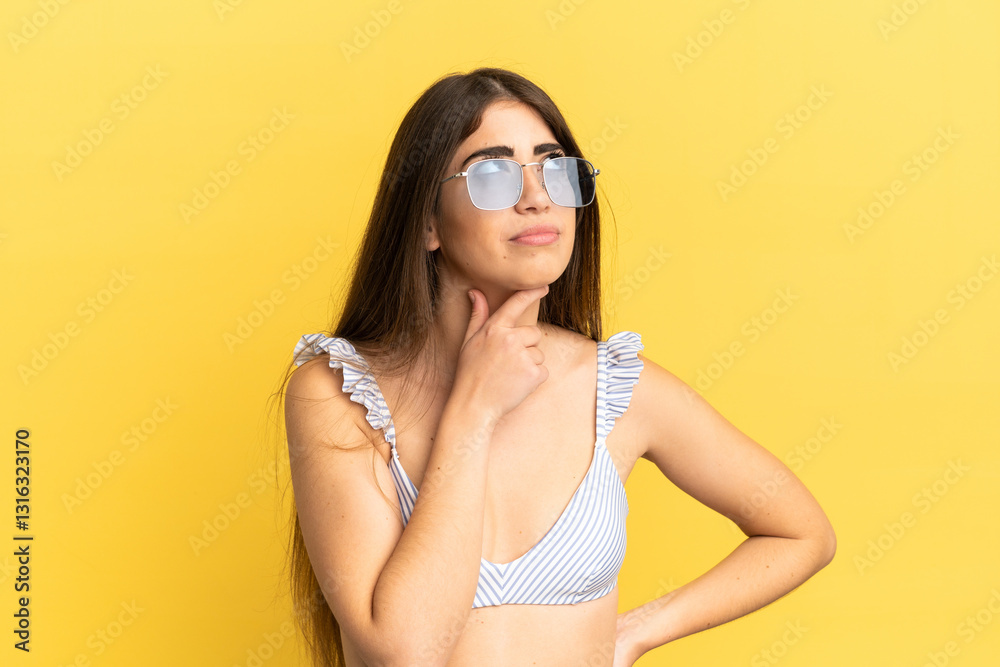 Young caucasian woman in swimsuit in summer holidays isolated on yellow background and looking up Young caucasian woman in swimsuit in summer holidays isolated on yellow background and looking up