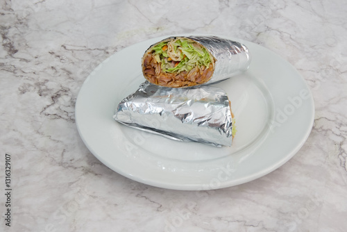 A silver foil wrapped burrito sits on a white plate