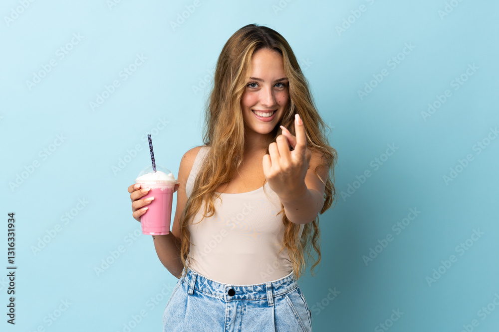 Young woman with strawberry milkshake isolated on blue background doing coming gesture Young woman with strawberry milkshake isolated on blue background doing coming gesture