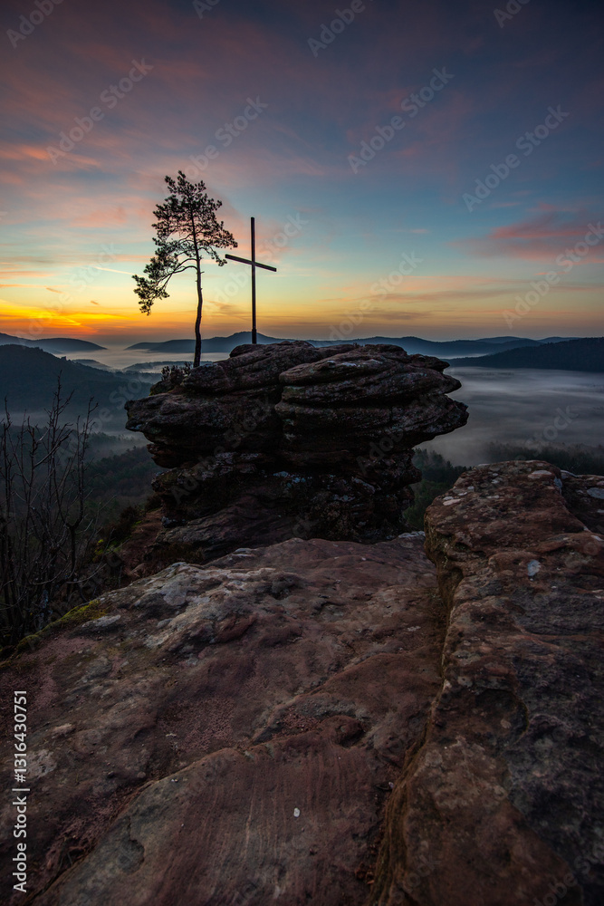 Summit cross on a sandstone rock in the middle of the forest. Landscape with a magnificent view over a forest shrouded in fog. Sunrise in the Palatinate Forest, Germany Summit cross on a sandstone rock in the middle of the forest. Landscape with a magnificent view over a forest shrouded in fog. Sunrise in the Palatinate Forest, Germany