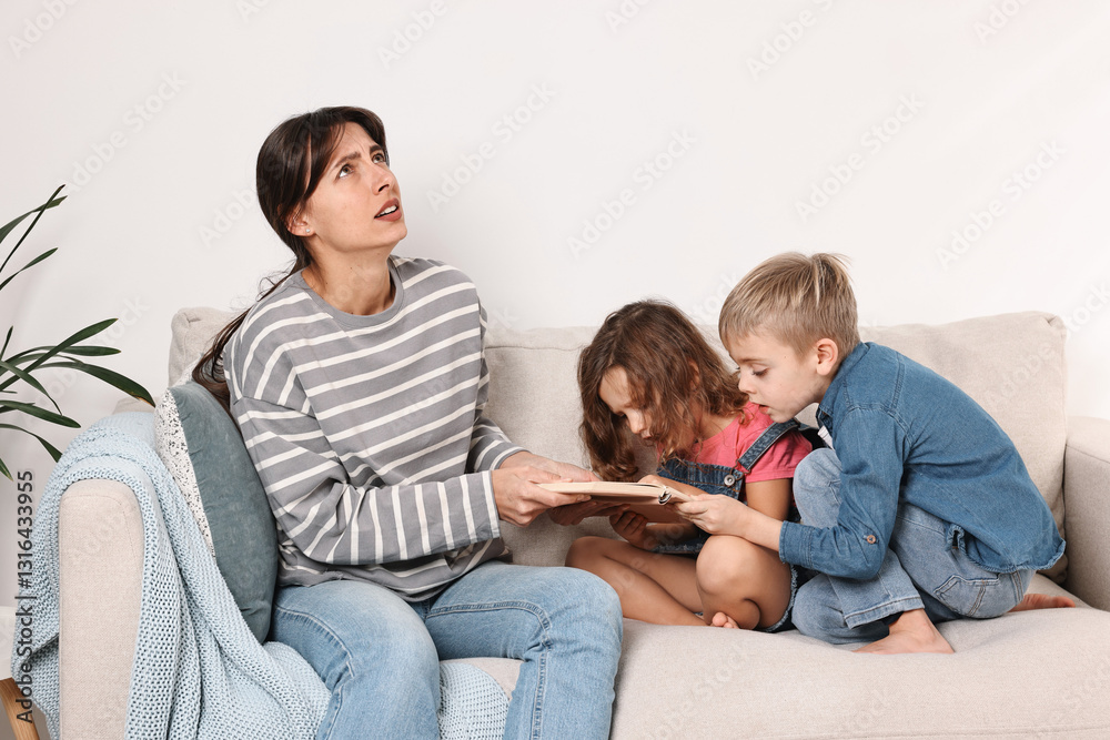 Overwhelmed mother and her naughty children with book on sofa at home Overwhelmed mother and her naughty children with book on sofa at home