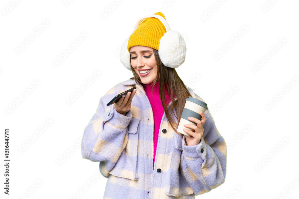 Young woman wearing winter muffs over isolated chroma key background holding coffee to take away and a mobile Young woman wearing winter muffs over isolated chroma key background holding coffee to take away and a mobile