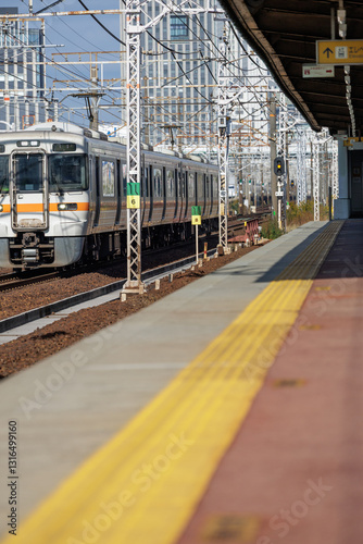 Japan Rush Hour - express commuter train passes by a non-stop station's platform devoid of commuters as it passes under a network of overhead power lines on its morning route.