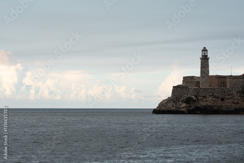 Castillo del morro lighthouse perched on rocky havana coastline, illuminating maritime heritage against expansive ocean backdrop with moody clouded horizon