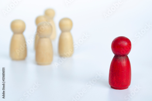 A wooden red doll separated by the rest non red wooden dolls. Discrimination or leadership concept