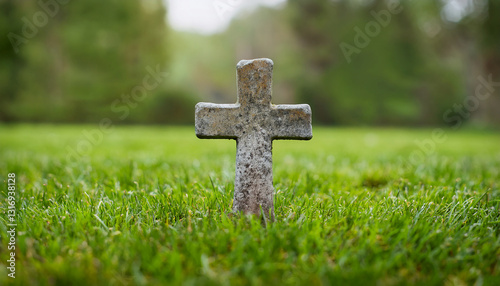 Weathered stone tombstone with Christian cross on lush green grass. Faith and remembrance.