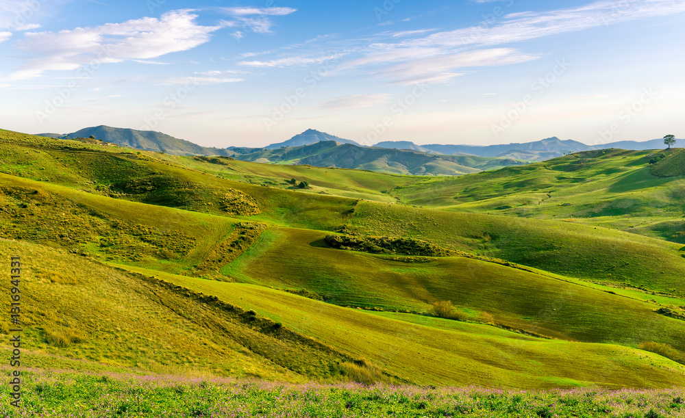 Obraz premium green spring season landscape of beautiful grassland hills in countryside with villages and mountains under scenic cloudy sky