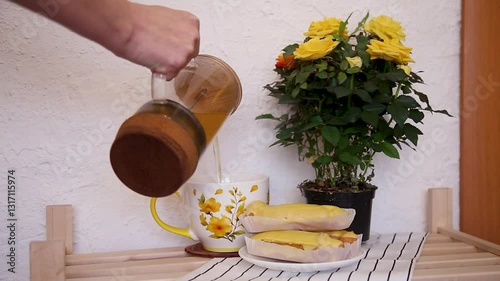 A woman's hand pours tea into a beautiful cup on a wooden table. Rustic style