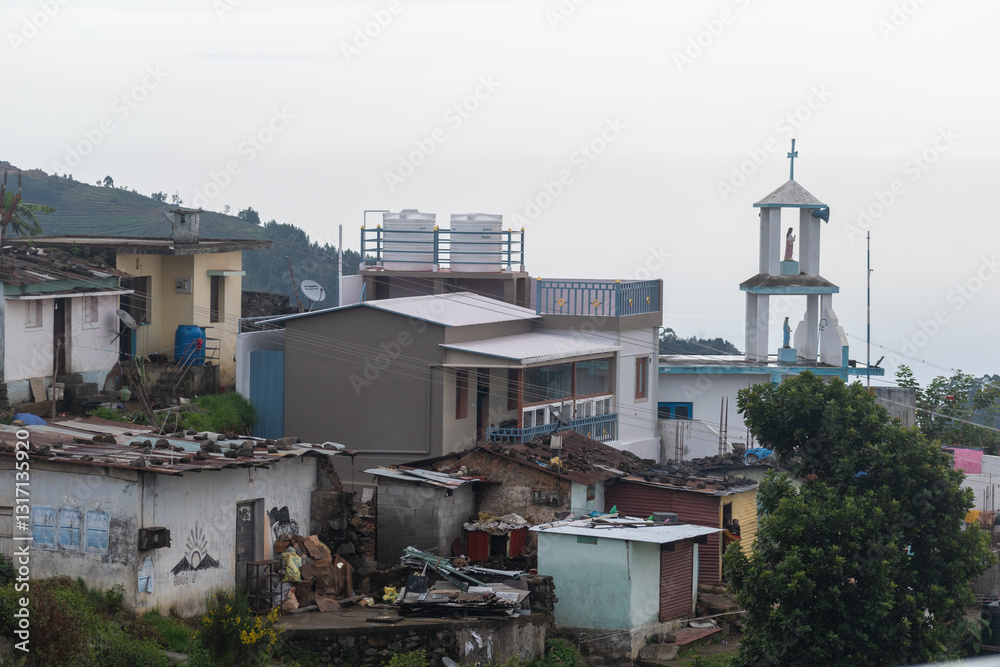 Obraz premium Nestled in Kodaikanal, the village showcases a blend of traditional and modern architecture. Houses are surrounded by lush greenery, while a church steeple rises against the morning sky.