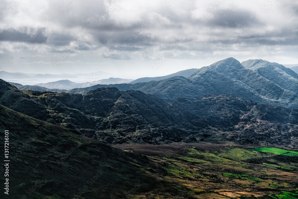 Obraz premium The Carrauntoohil Trail in Ireland, taking in breathtaking scenery of rugged hills and vibrant green fields under dynamic cloudy skies.