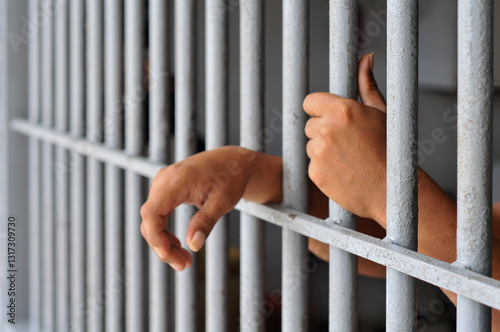 prisoner's hands behind bars with black background	
