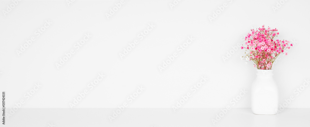 Bouquet of colorful pink babys breath flowers on a white shelf against a white wall. Copy space.