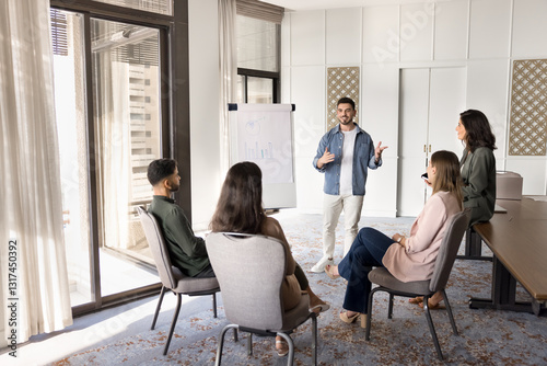 Young Arabian business coach making flip chart presentation standing in front of staff members, presenting idea, explain meeting goals, reviewing project updates, planning upcoming tasks and strategy