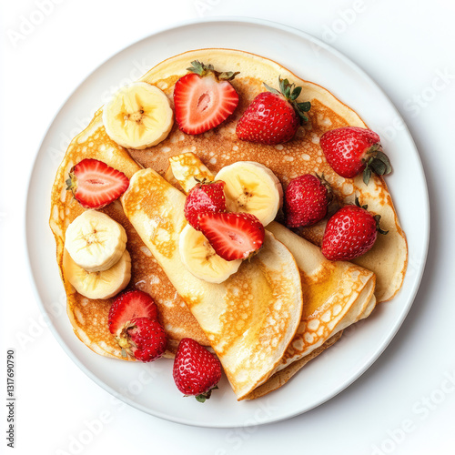 Overhead view of pancakes topped with sliced bananas and strawberries on a white plate
