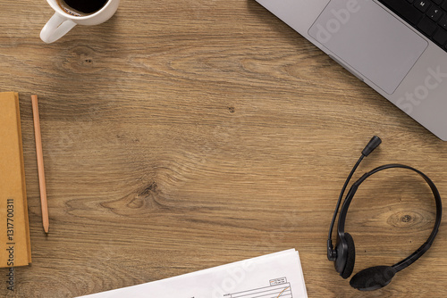 Obraz na płótnie Top view of a wooden office desk with a laptop, coffee, headset, documents, and a notebook. A modern workspace setup for remote work, customer support, or online communication w salonie
