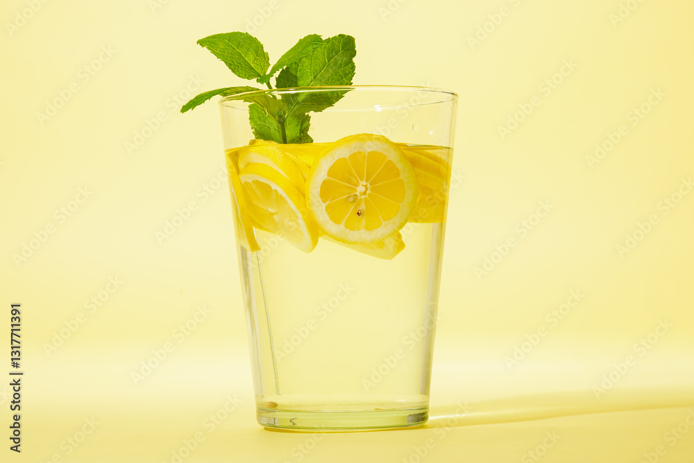 Glass of lemonade with mint against yellow background.